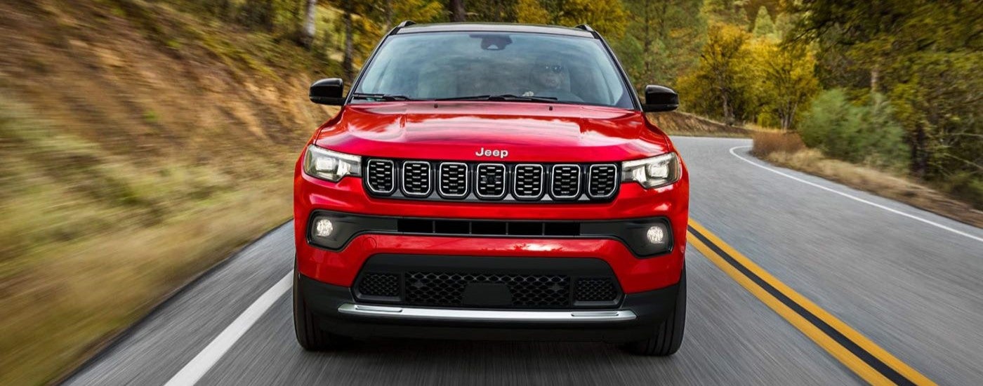 A red 2024 Jeep Compass shown head-on driving a paved road.