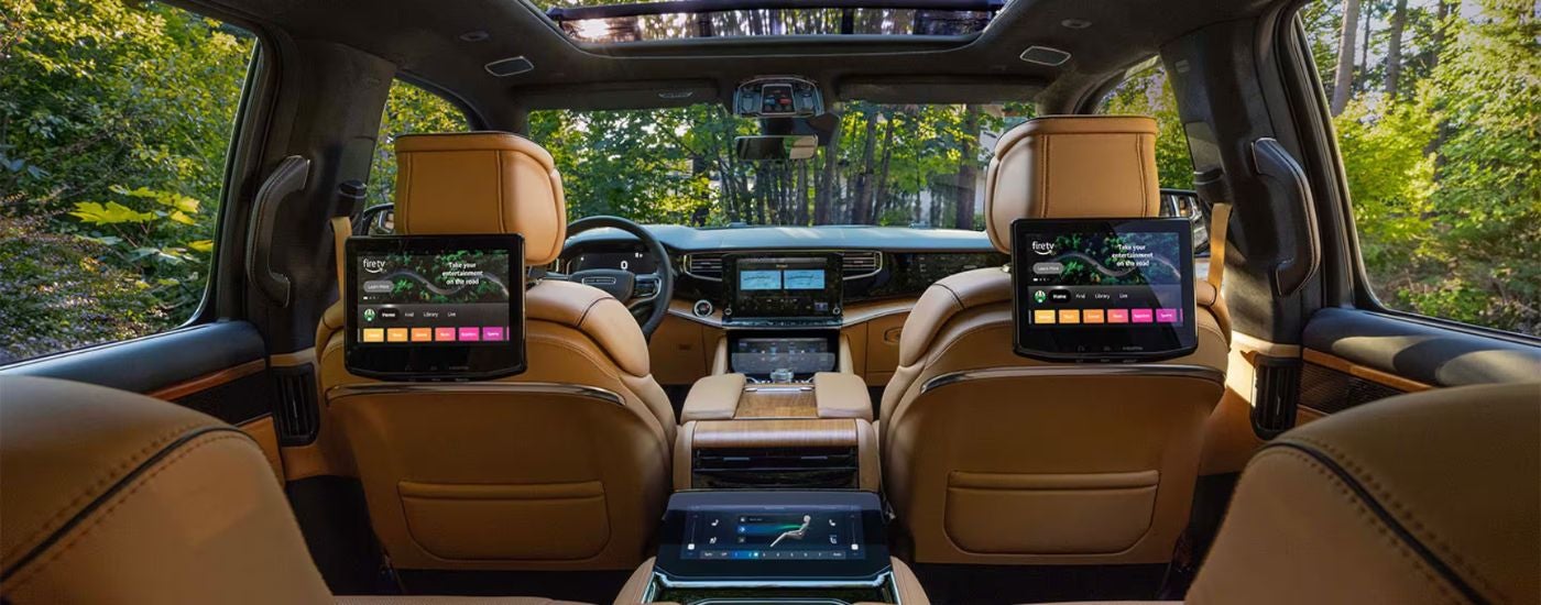 The brown leather interior of a 2026 Jeep Grand Wagoneer showing passenger entertainment screens.