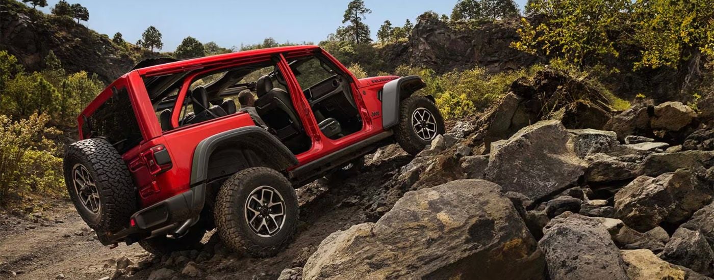 Red 2026 Jeep Wrangler driving up a pile of rocks.